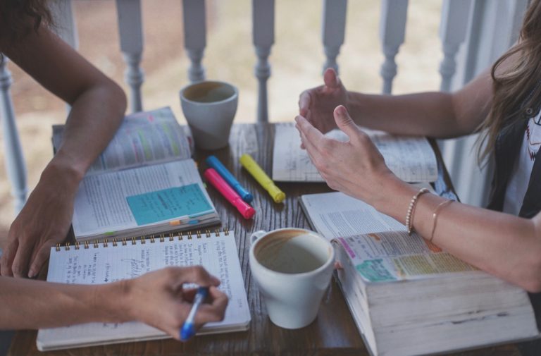 Detail of two girls talking over open bibles and notebooks.