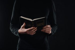 cropped shot of priest reading holy bible isolated on black